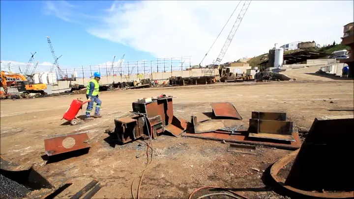 A ship dismantling yard with cranes, steel sections and a worker wheeling a cylinder.