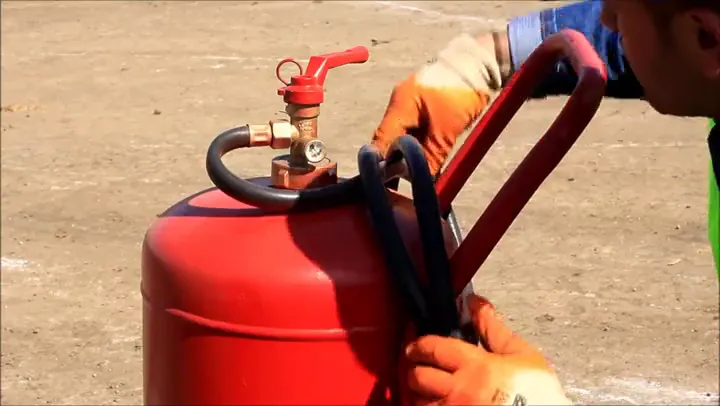Gloved hands open the valve on a red gas cylinder in a ship dismantling yard.
