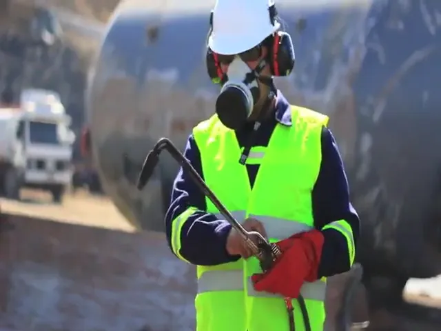 A worker in a hi-vis vest, respirator and hard hat holds a cutting torch.